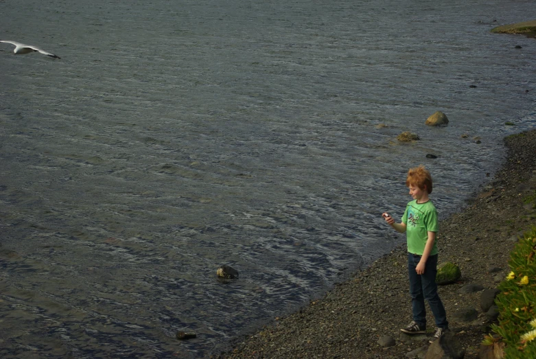 a little boy is standing by the water and looking at his phone