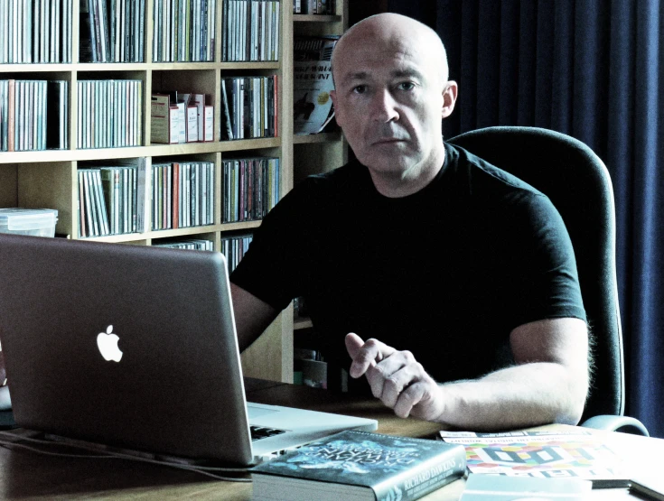 a bald man sitting at his desk in front of a computer