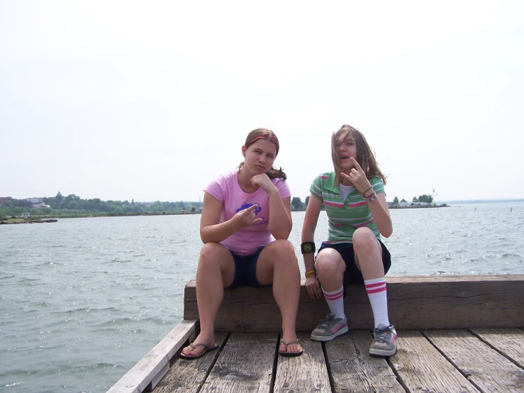 two women sitting next to each other on a dock