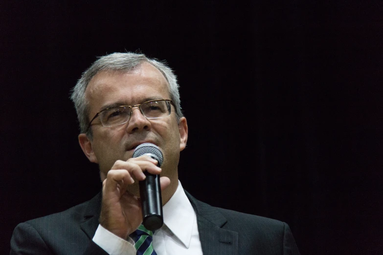 a man is talking into a microphone in front of a crowd