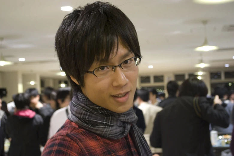 a man with glasses and a scarf in a room full of people