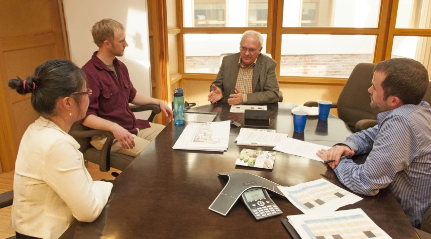 five people sit around a conference table talking and looking at paperwork