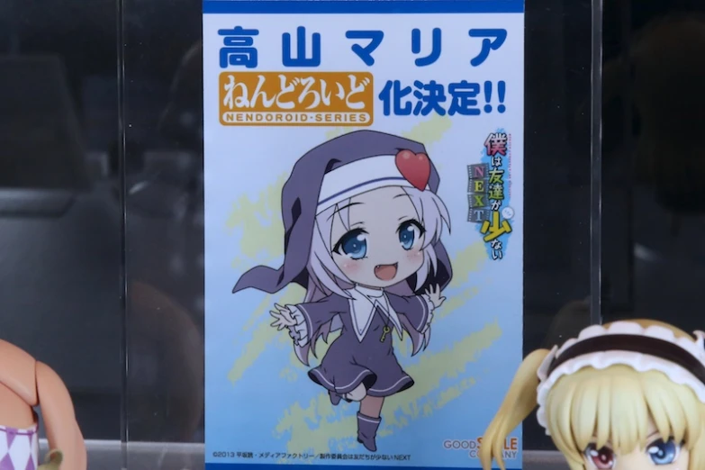 two anime dolls stand near a poster