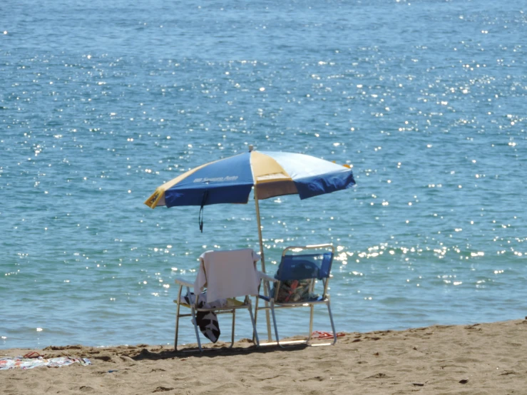 chairs are on the beach under an umbrella