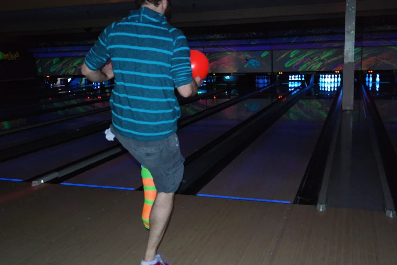 a young man wearing an orange bowling ball at a bowling alley