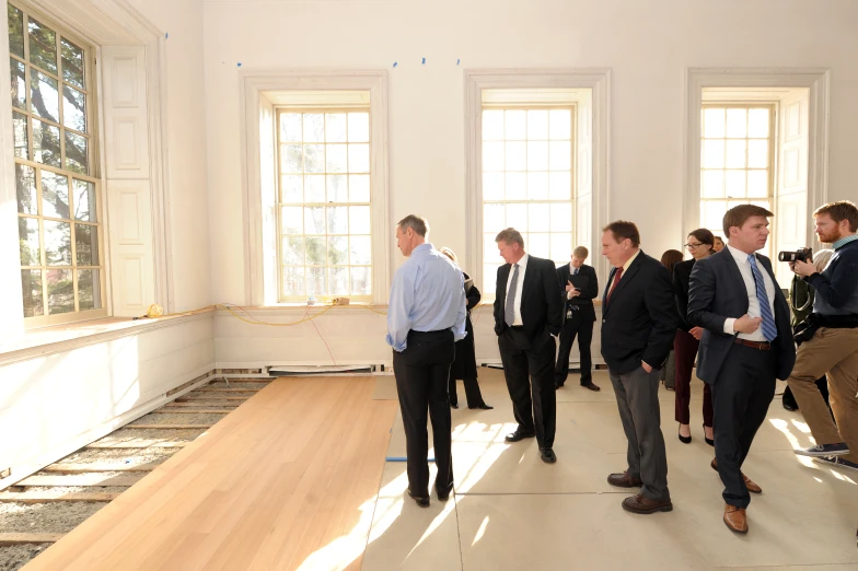 group of men dressed in suits standing next to each other in a large room with three windows