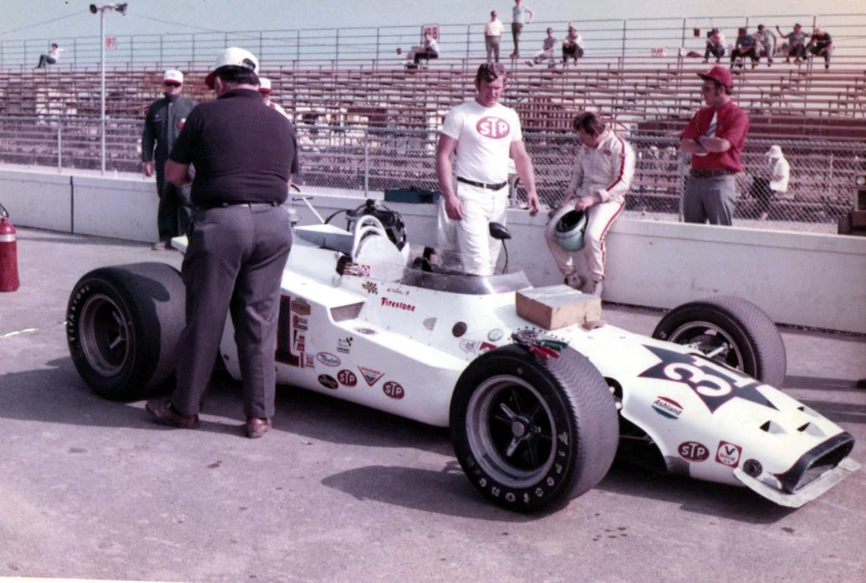 a man standing on the front of a race car in front of people