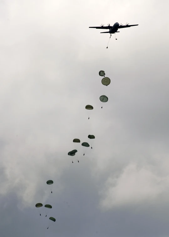 military parachutes being flown in formation as a plane flies in the background