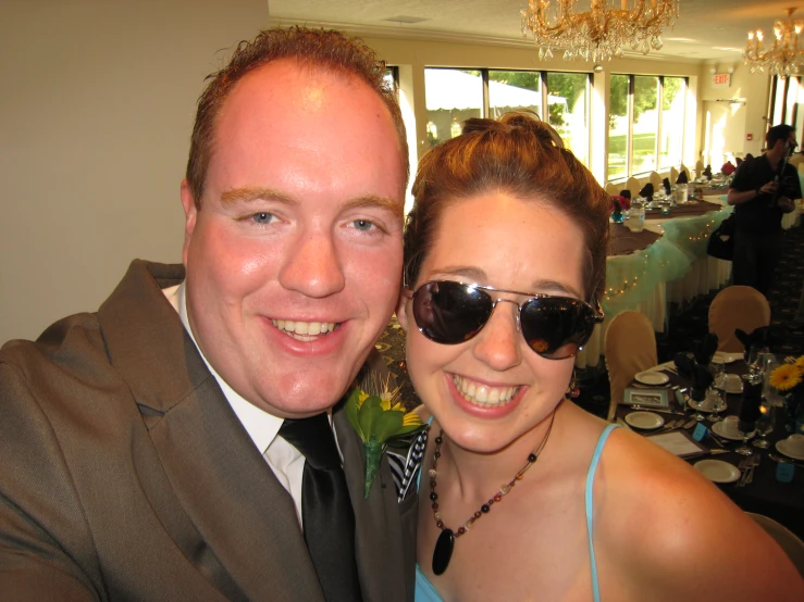 a man in suit and tie standing next to a woman wearing sunglasses