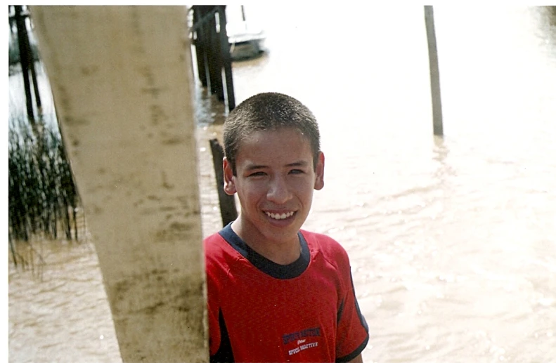 a boy standing by the water in a red shirt