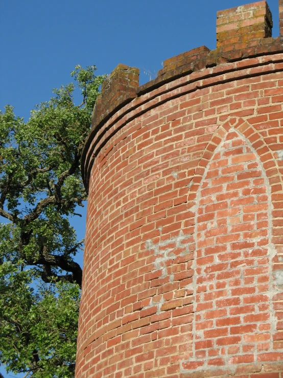 the clock on the side of a brick tower with a tree