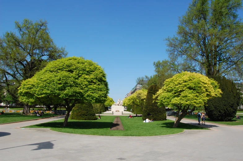 people walk through an open park with trees and flowers