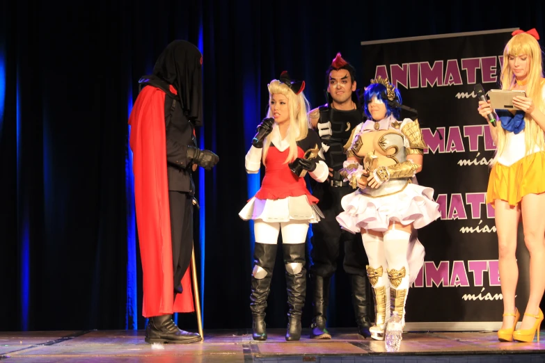 four women in costumes stand on stage as two of them look towards the camera