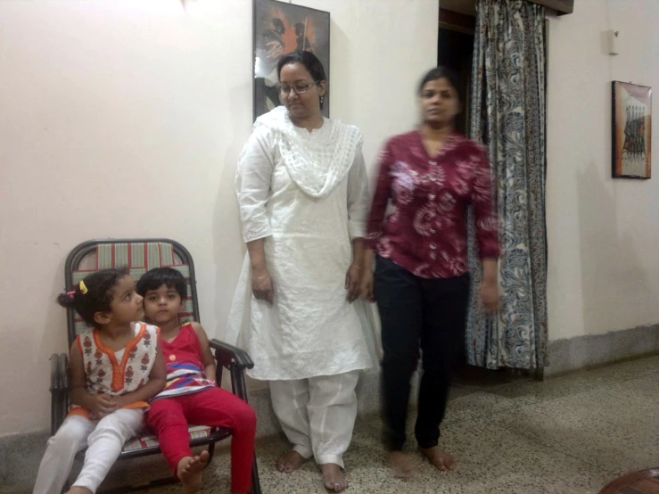 two ladies in white standing beside a child on a chair