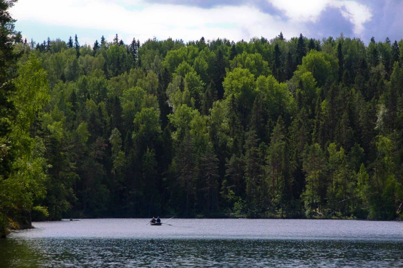 a small boat is in the middle of a lake surrounded by trees