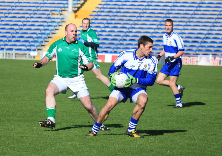 three men on a field playing soccer with one going to the ball