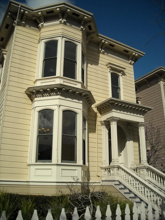 an old victorian home is painted off cream with white trim