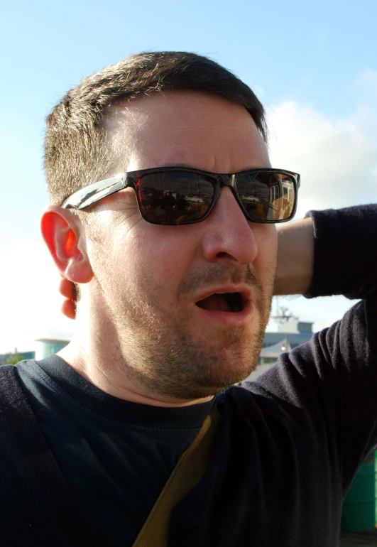 a man wearing sunglasses holds his head near his ear