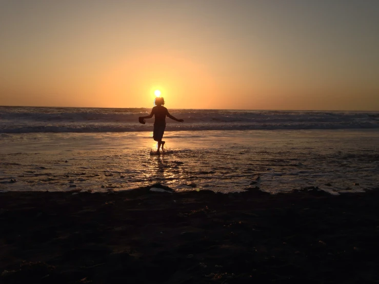 the person walking into the ocean at sunset