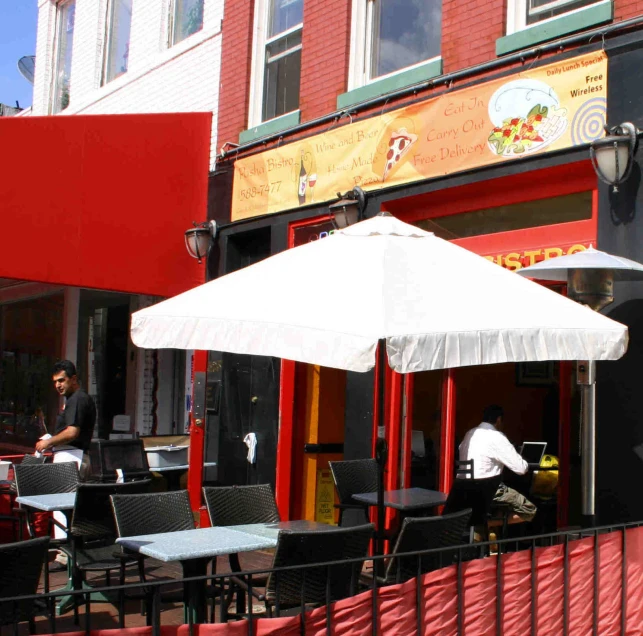 the outside of a restaurant with tables, chairs and umbrella