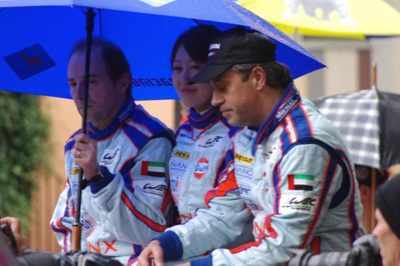 three race track officials sitting under an umbrella