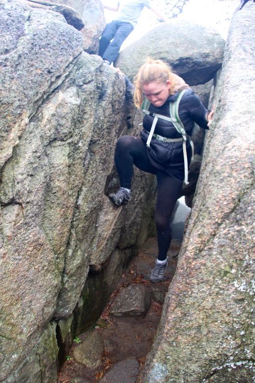 a woman climbing up a large rock face on a trail