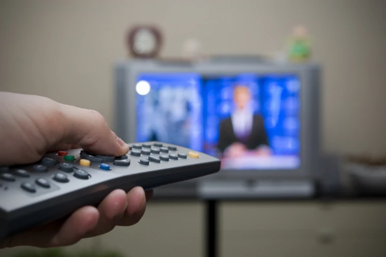 a hand holding a remote control in front of television