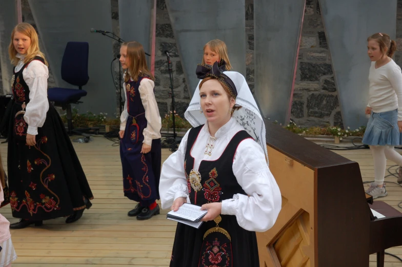 a girl in a dress holding a book is standing near other children