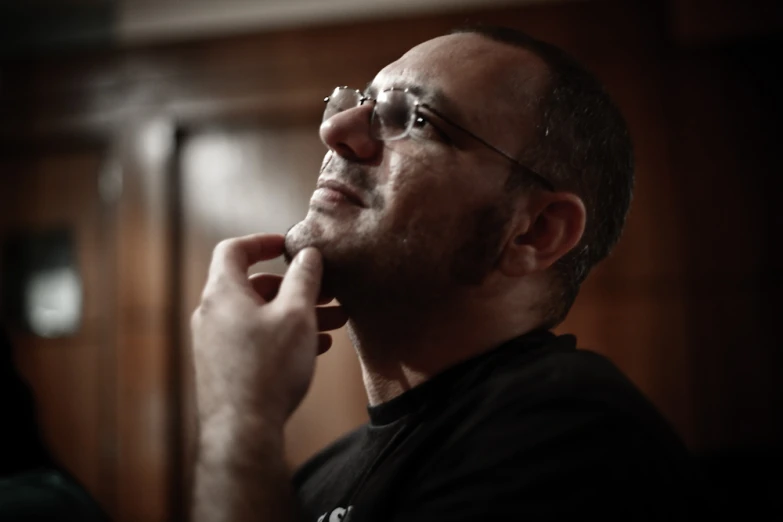 a man with glasses on in the dark looking off into the distance