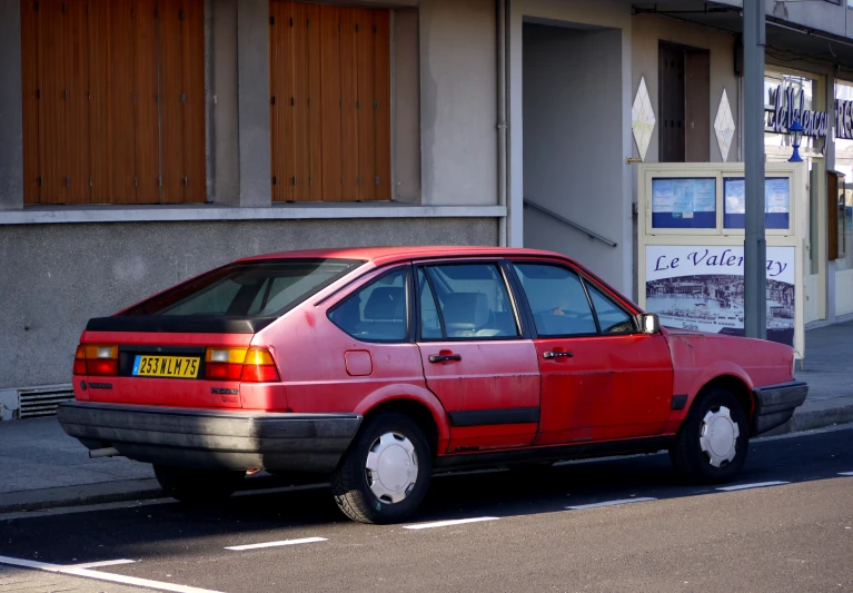 a red car sitting outside of a tan building