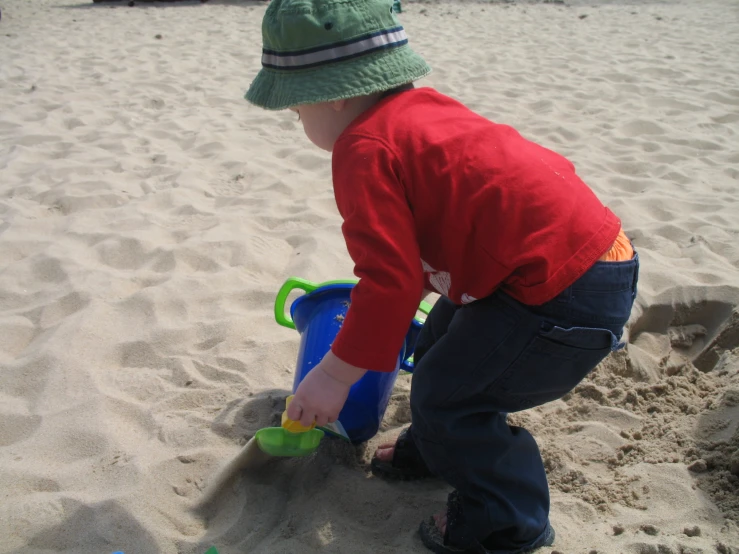 a little boy playing in the sand with his blue toy