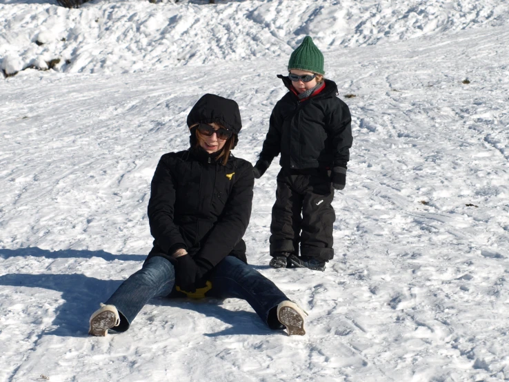 two s standing and sitting on the ground in the snow