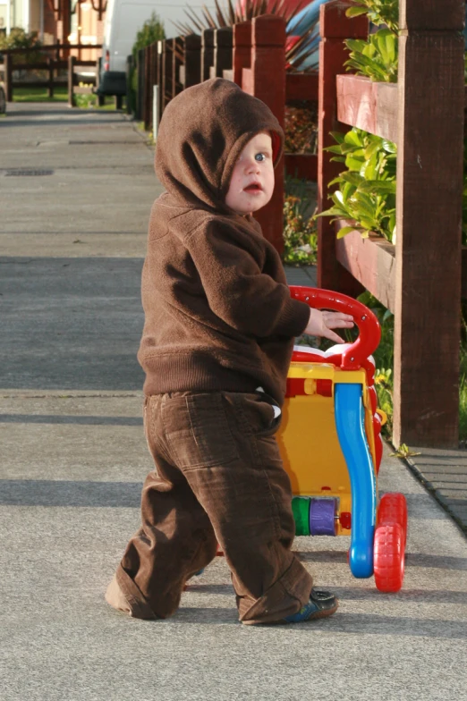 a child is in a brown outfit hing a toy cart