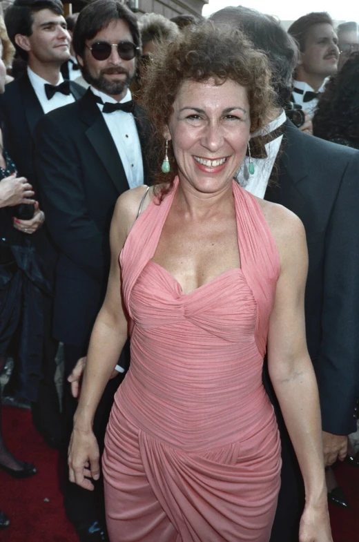 a woman in a pink dress smiling while wearing a tuxedo