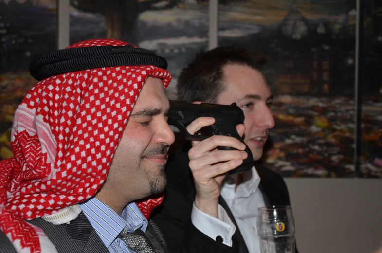 two men wearing red and white headscarves hold camera