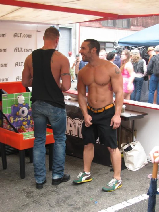 two men with their shirts off standing in front of a counter at a fair