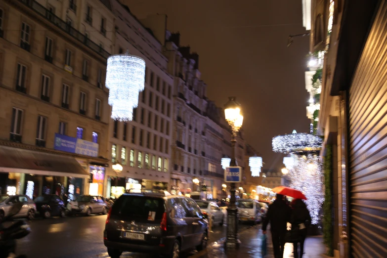 people on sidewalk next to tall building with buildings lit up