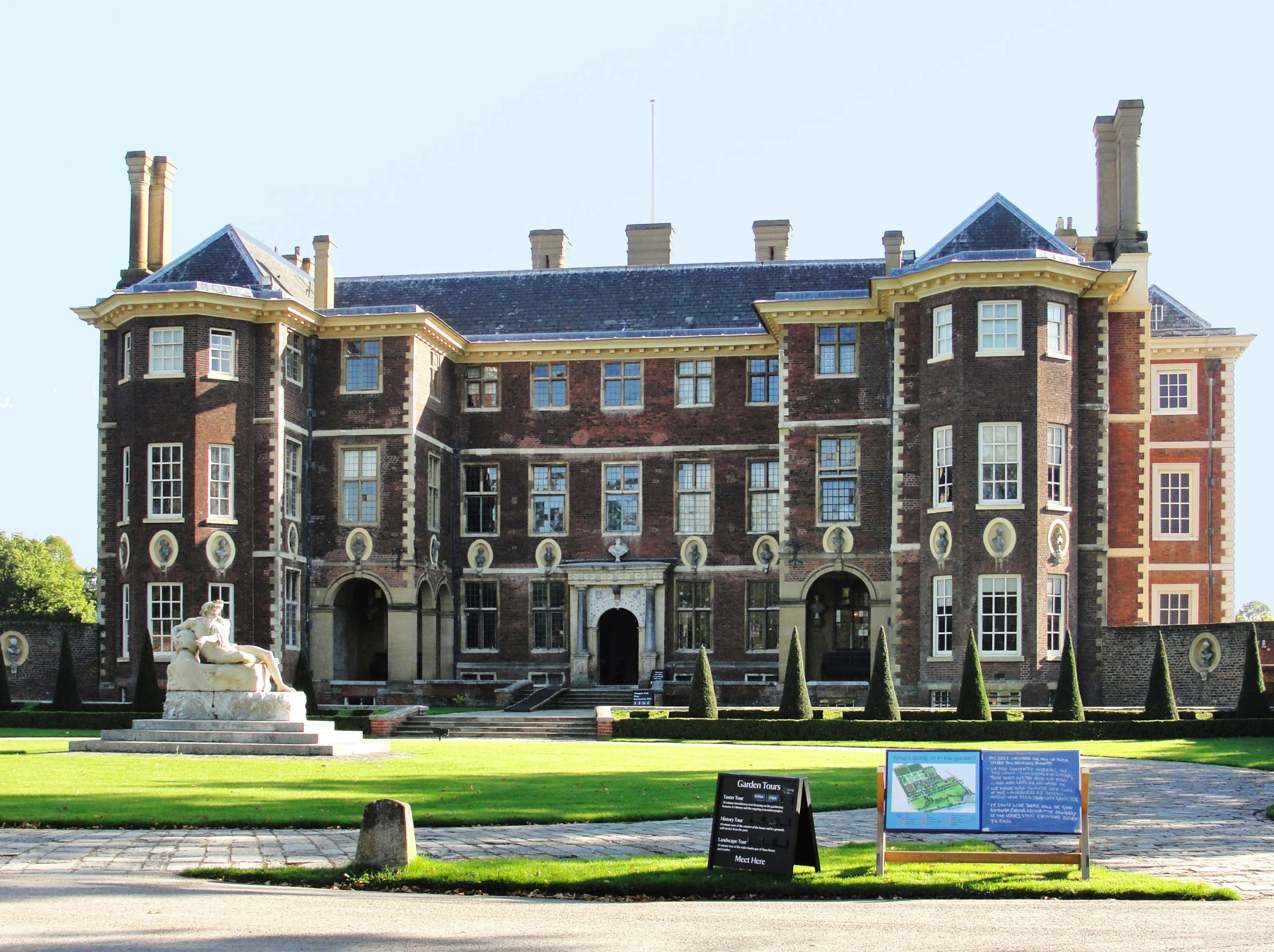 an old brick building with lots of windows and a statue on the grass