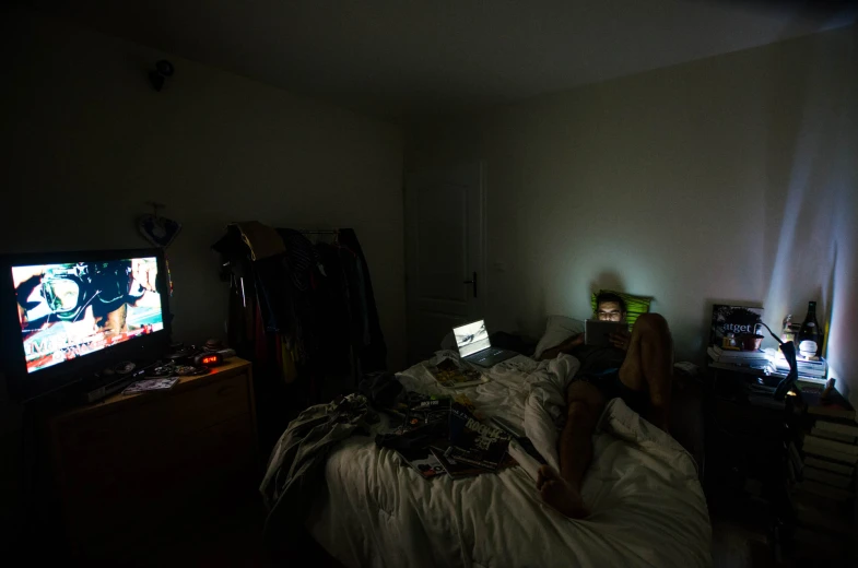 a person laying on their bed watching two tvs