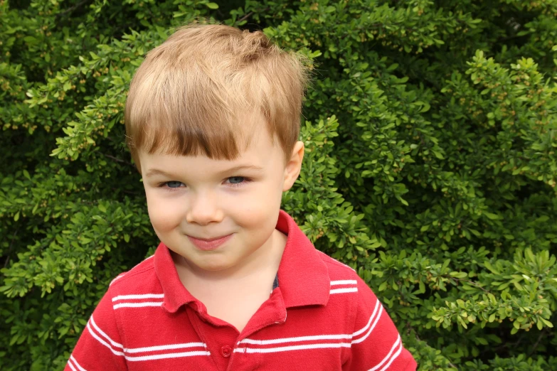 this little boy smiles in front of some bushes