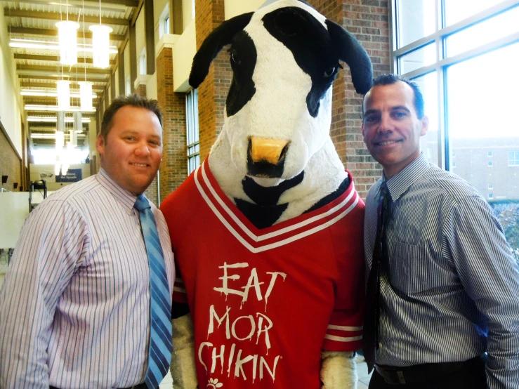 two men stand in front of a large mascot wearing a shirt that says eat more china