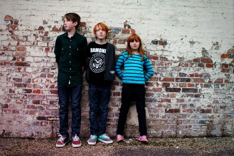 three little s standing next to a brick wall