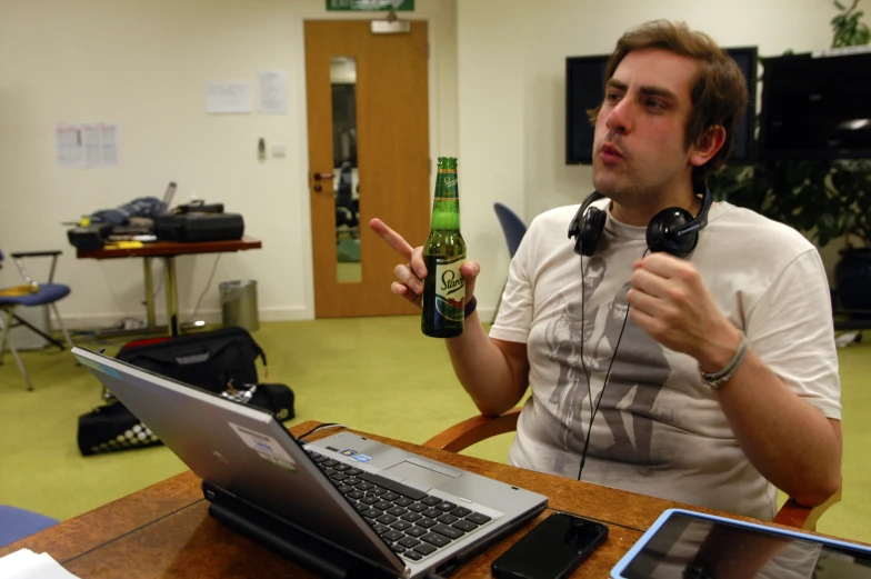 a man with headphones is drinking beer and using a laptop