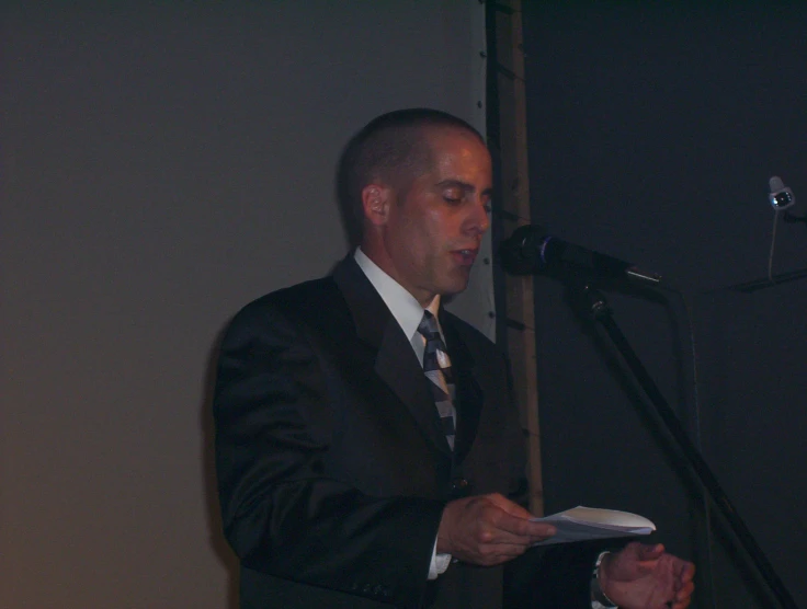 a man in a suit and tie reading from a paper