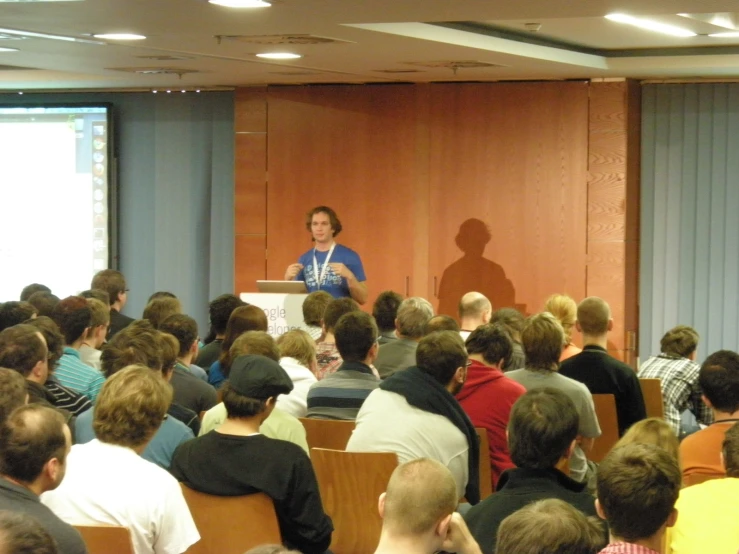 a woman stands in front of a large crowd, presenting