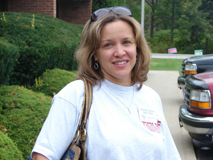 a smiling woman stands on the side walk with her handbag in her pockets