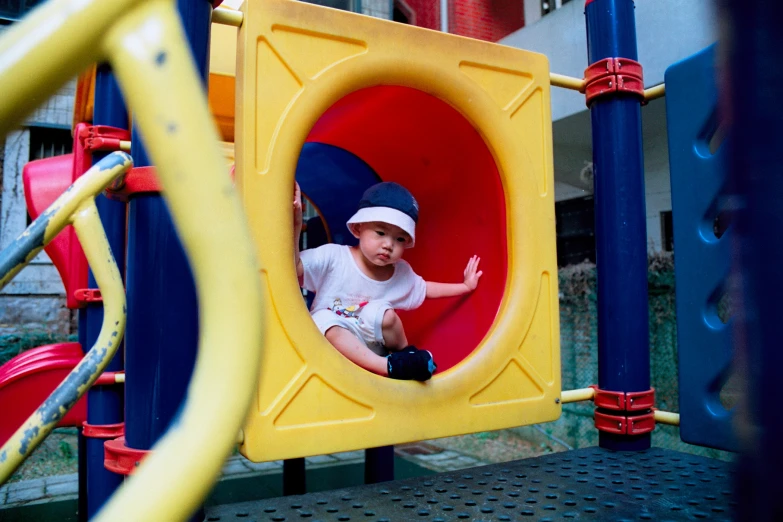 a  in white shirt sitting inside a yellow playground structure