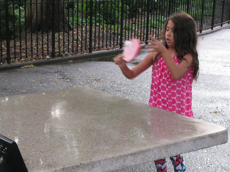 a small girl playing with her pink object in the rain