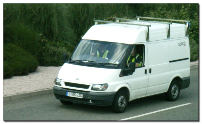 a white van driving down a street near trees