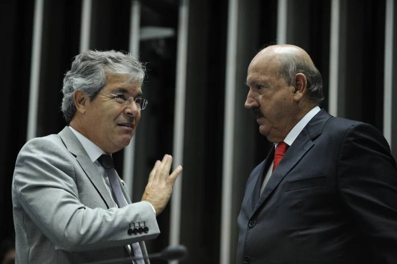 two men in suits talking with one holding his chin